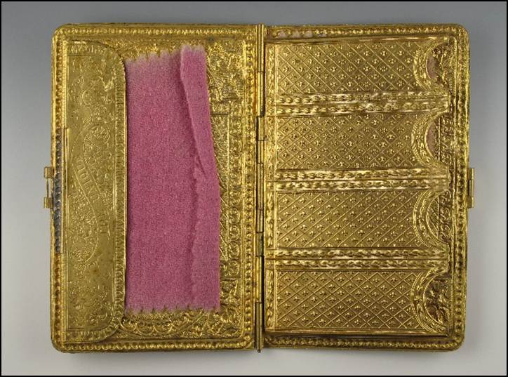 A gold cigarette case with pink fabric inside
Description automatically generated